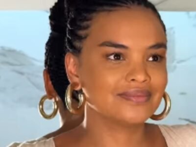 Lucy Ramos sorrindo em close, de brinco de argola dourado e trancas