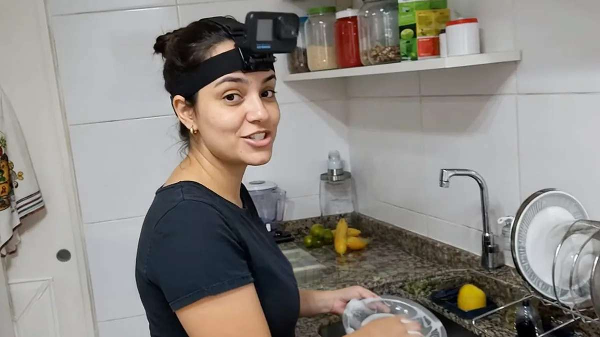 Mulher com câmera presa à testa por faixa de cabeça, lavando louça numa cozinha