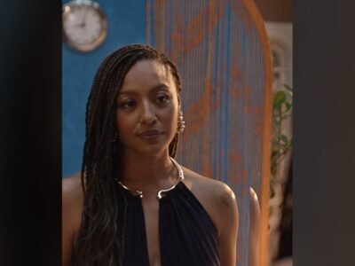 Sheron Menezzes como Isabela em cena da novela Por Você, de vestido escuro, diante de uma porta azul