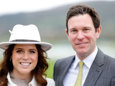Princesa Eugenie de chapéu branco ao lado de Jack Brooksbank, de terno cinza, os dois sorrindo