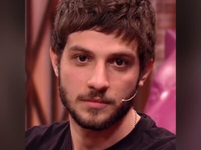 Chay Suede em close, de camiseta preta e microfone de lapela, olhando para frente