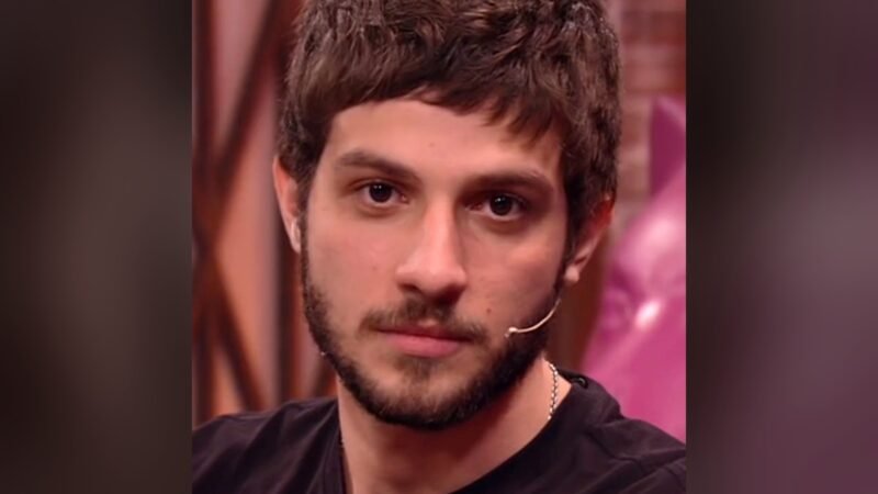 Chay Suede em close, de camiseta preta e microfone de lapela, olhando para frente