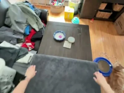 Imagem em primeira pessoa de mãos dobrando roupa sobre uma mesa, gravada por câmera na altura dos olhos