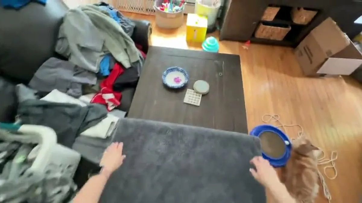 Imagem em primeira pessoa de mãos dobrando roupa sobre uma mesa, gravada por câmera na altura dos olhos