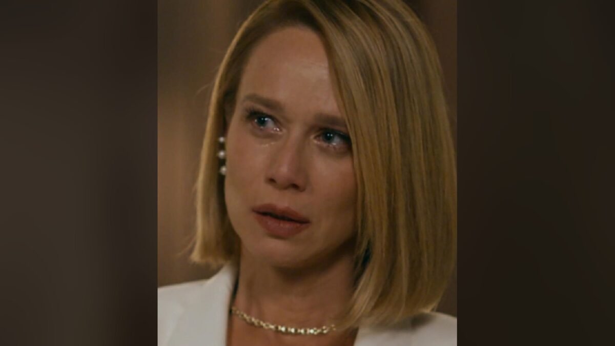 Mariana Ximenes como Dora, de blazer branco e olhos marejados, em close de cena de Quem Ama Cuida