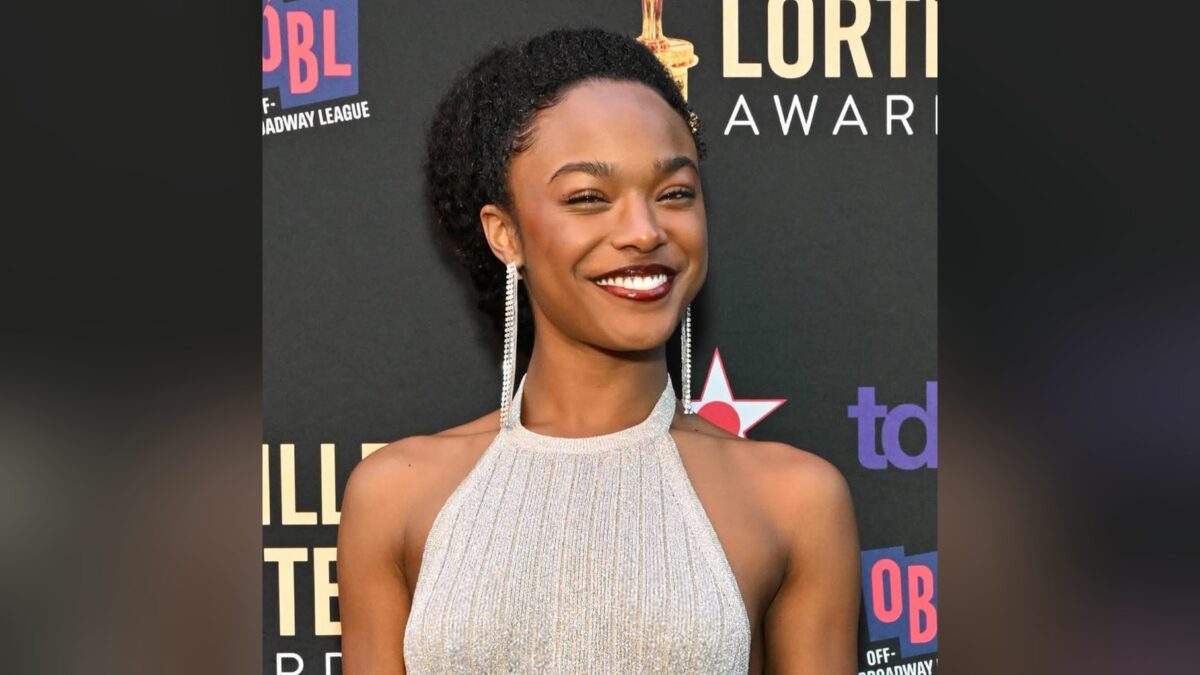 Maya Boyd sorrindo, de vestido prateado e brincos longos, no painel do Lucille Lortel Awards