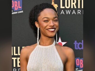 Maya Boyd sorrindo, de vestido prateado e brincos longos, no painel do Lucille Lortel Awards