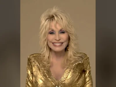 Dolly Parton, de vestido dourado, sentada e sorrindo para a câmera