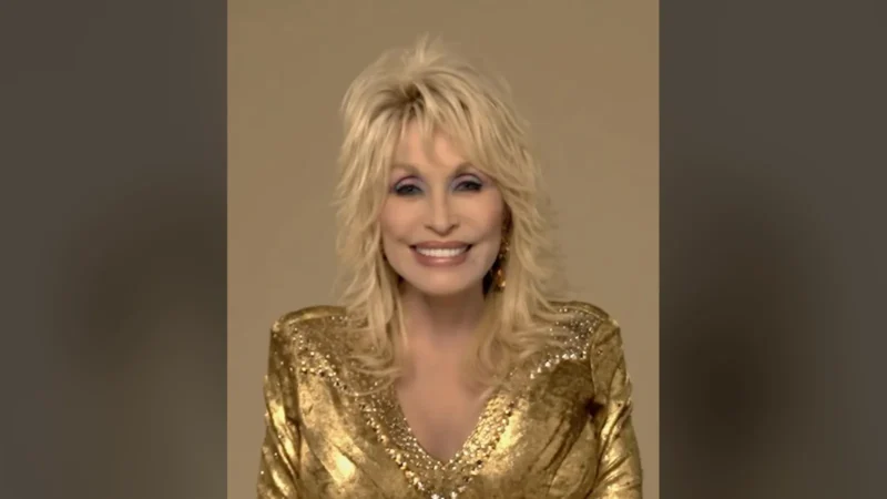 Dolly Parton, de vestido dourado, sentada e sorrindo para a câmera