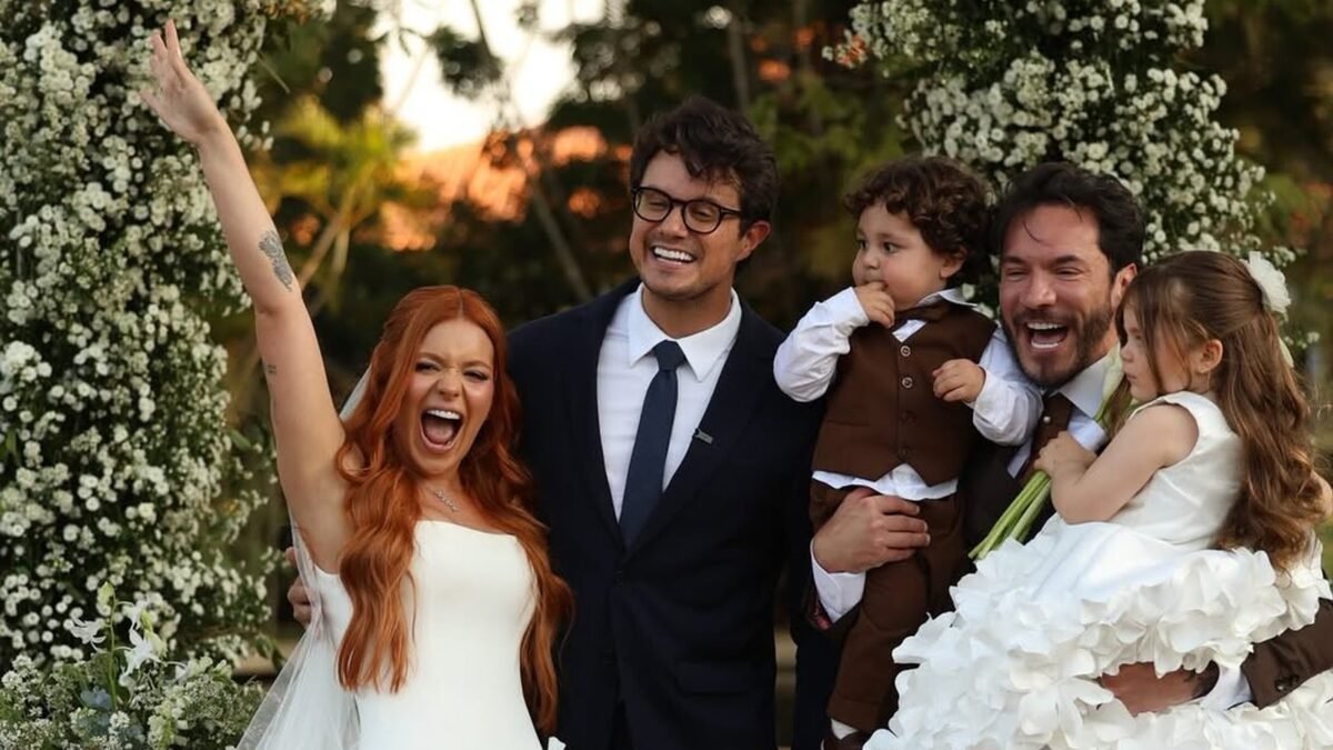 Viih Tube de vestido de noiva branco e Eliezer de terno, com os filhos Lua e Ravi, sob o arco de flores da cerimônia