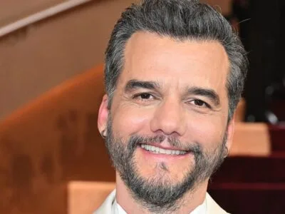 Wagner Moura de barba grisalha e terno claro, sorrindo em evento