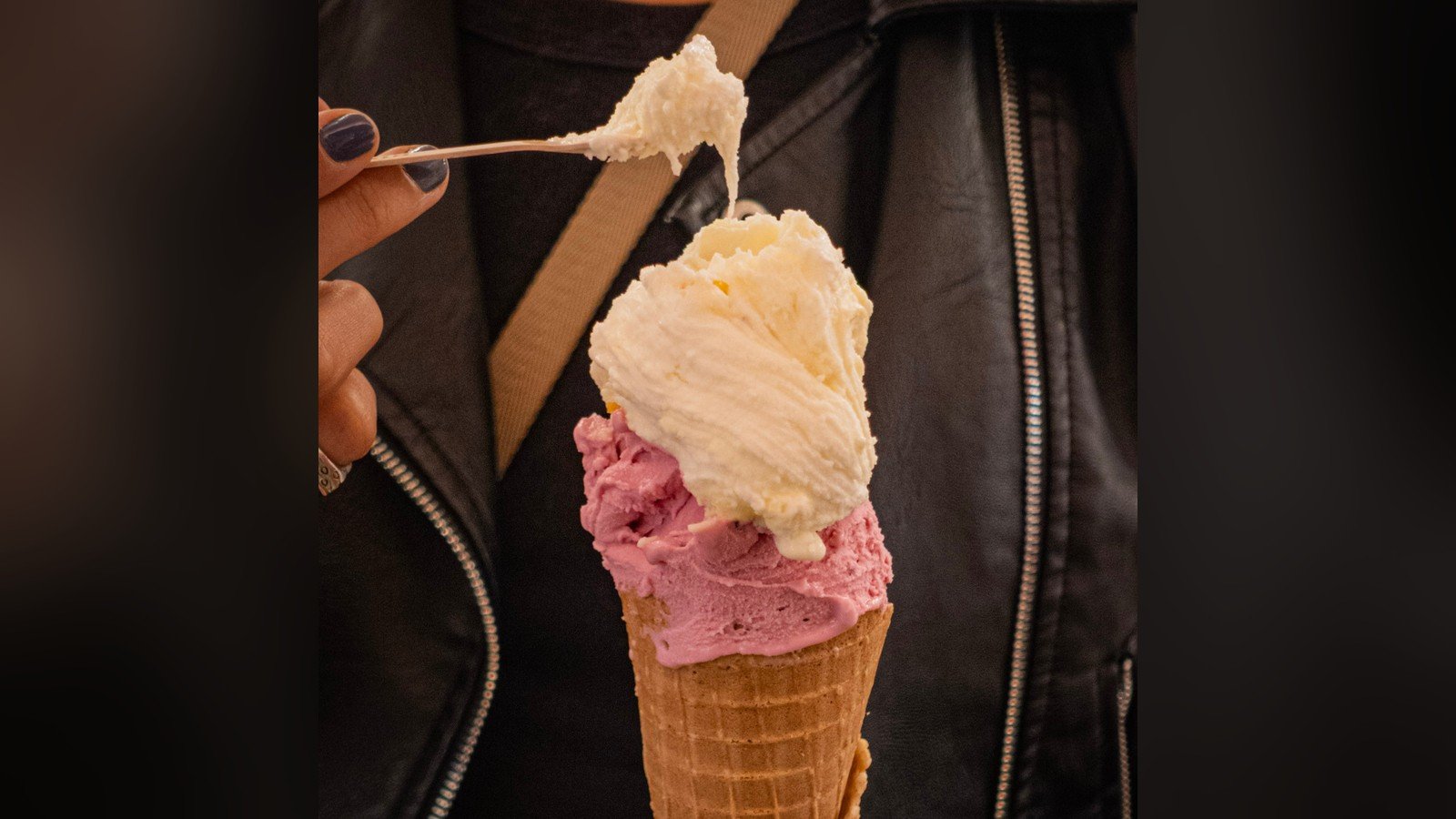 Casquinha com uma bola rosa e uma bola clara de gelato, segurada diante de uma jaqueta de couro