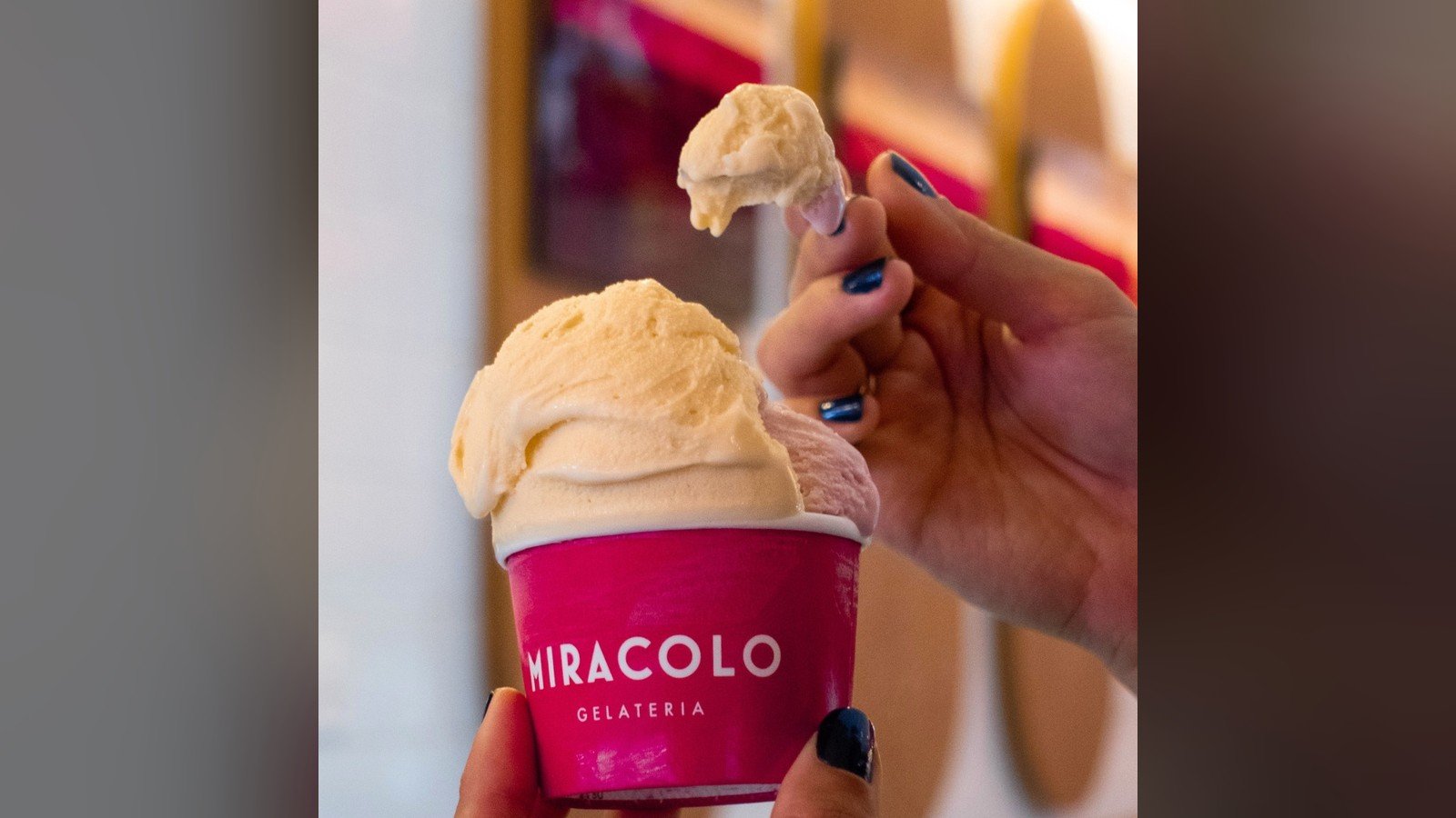 Copo rosa da Miracolo com duas bolas de gelato, segurado por duas maos