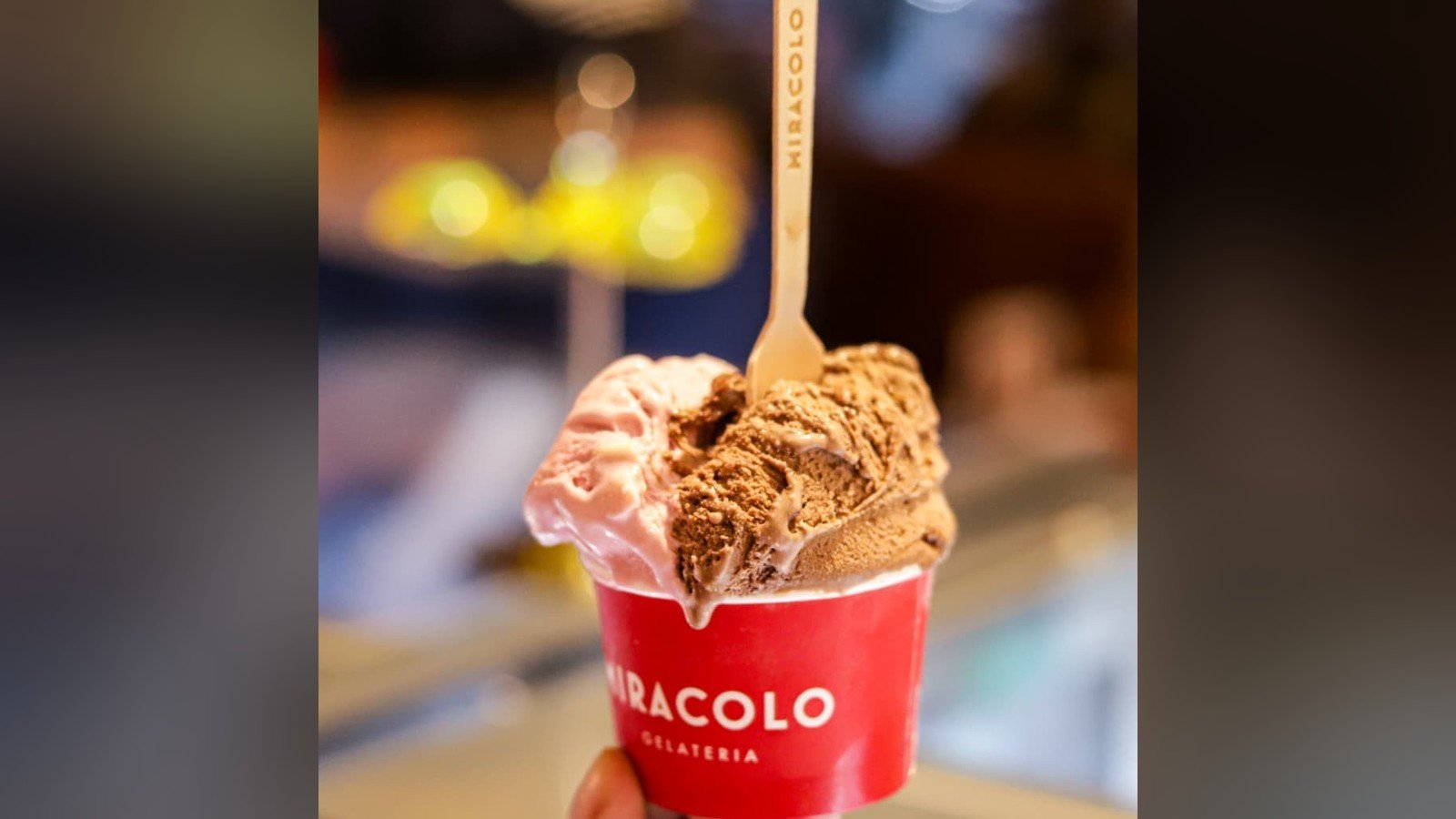 Copo vermelho da Miracolo com gelato de chocolate e de morango e uma colher de madeira