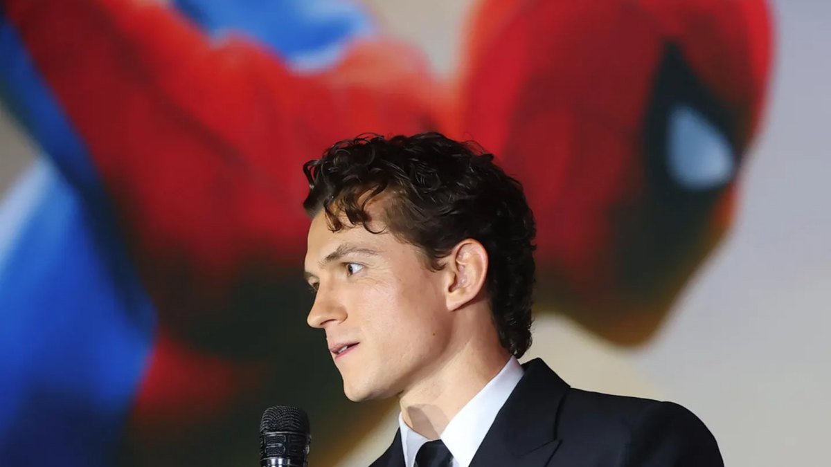 Tom Holland fala à imprensa diante de uma arte do Homem-Aranha.