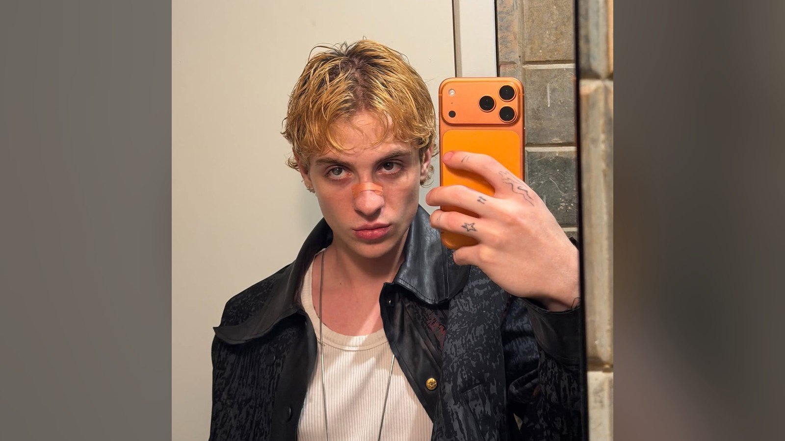 Juliano Floss, de cabelo loiro e jaqueta escura, faz selfie diante de um espelho