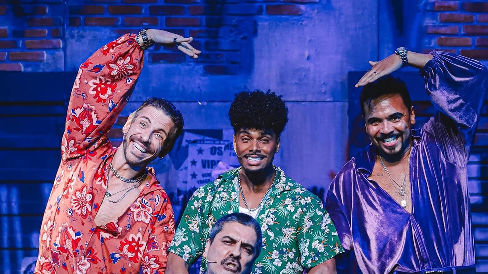 Atores de camisas coloridas em cena de musical num palco com cenario de rua