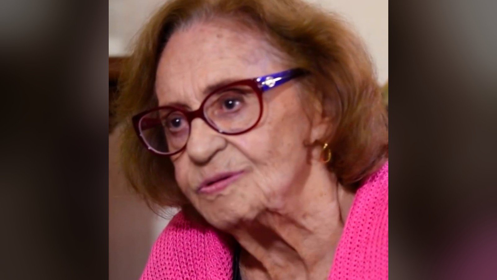 Laura Cardoso de cardiga rosa e oculos vermelhos, sorrindo durante entrevista em 2019