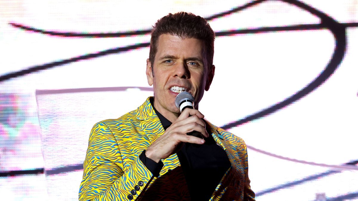 Perez Hilton fala ao microfone num palco iluminado.