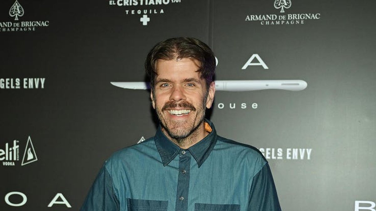Perez Hilton sorri em painel de patrocinadores.