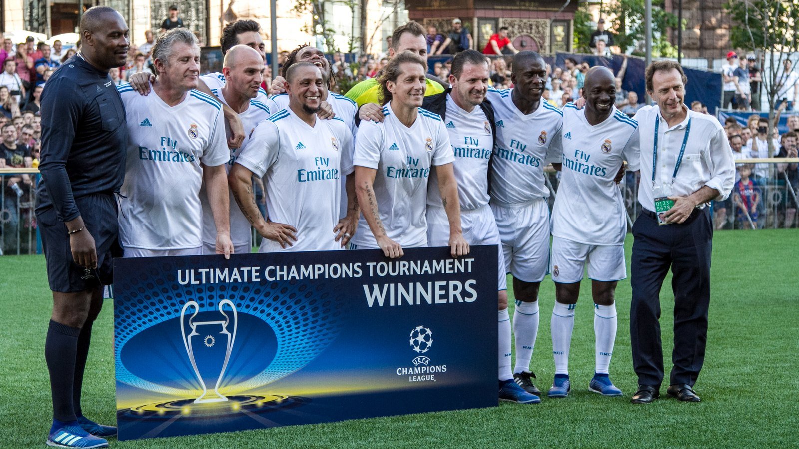 Roberto Carlos entre ex-jogadores de branco do Real Madrid, atras de um banner de torneio de lendas em 2018
