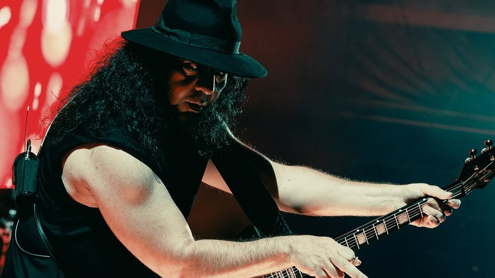 Guitarrista do System of a Down de chapeu preto toca sob luz vermelha durante show