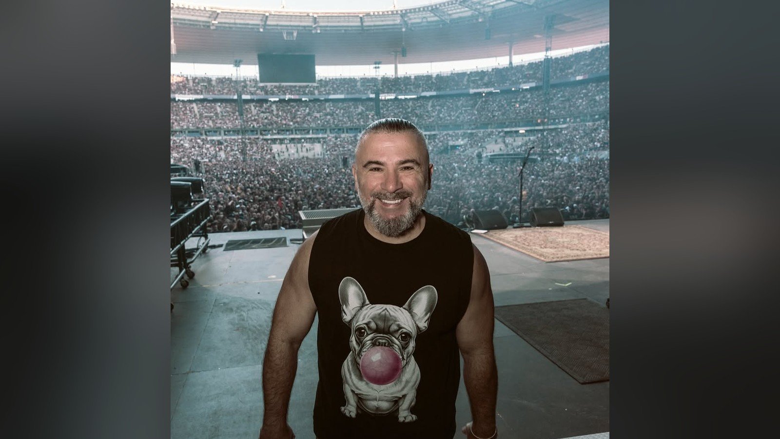 Integrante do System of a Down em pe no palco de um estadio lotado, visto de tras da plateia