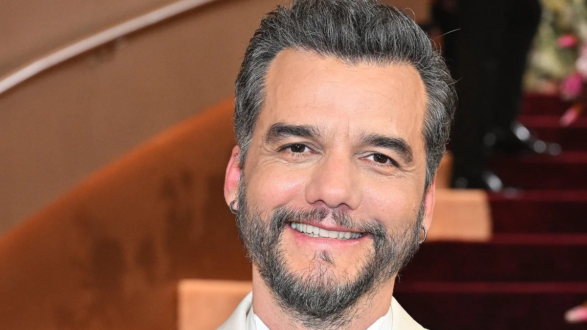 Wagner Moura sorri, de barba grisalha, em tapete vermelho.
