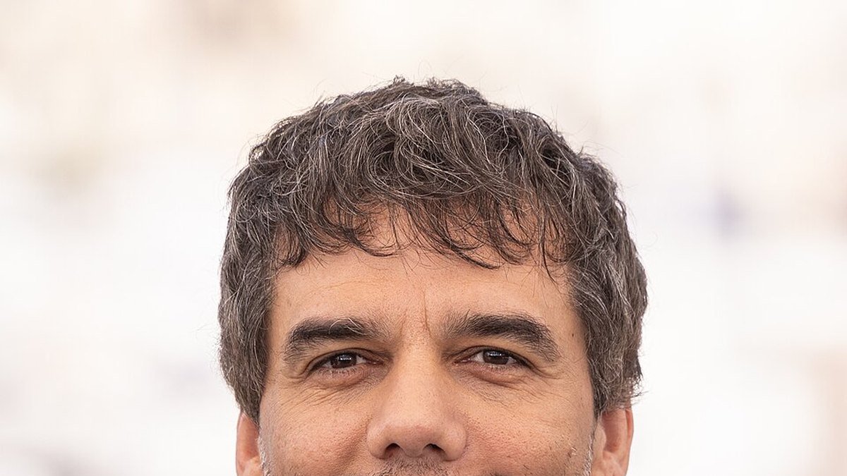 Retrato de Wagner Moura de cabelo grisalho, ao ar livre.