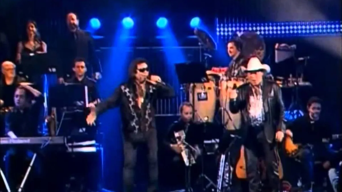 José Rico, de óculos escuros e cabelo comprido, e Milionário, de chapéu branco, cantando no palco diante da banda