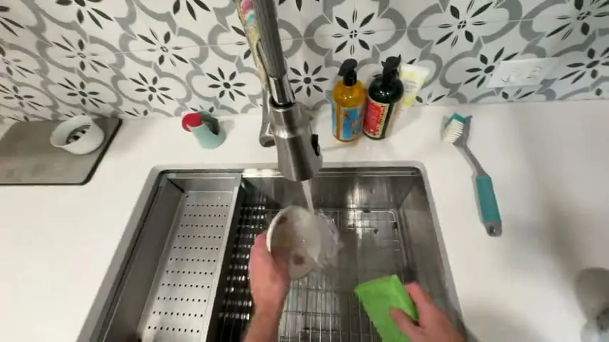 Imagem em primeira pessoa de mãos lavando louça numa pia cheia, gravada por câmera na altura dos olhos