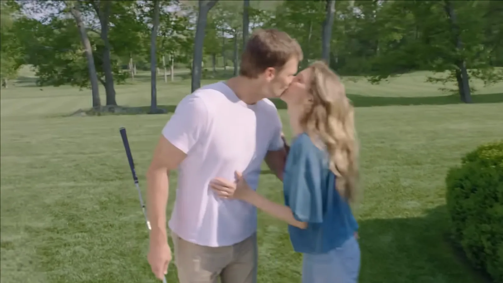 Tom Brady, de camiseta branca e taco de golfe na mão, beija Gisele Bündchen, de blusa azul, no jardim de casa