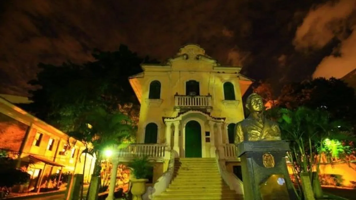 Fachada do Retiro dos Artistas iluminada à noite, com escadaria e um busto em frente ao prédio