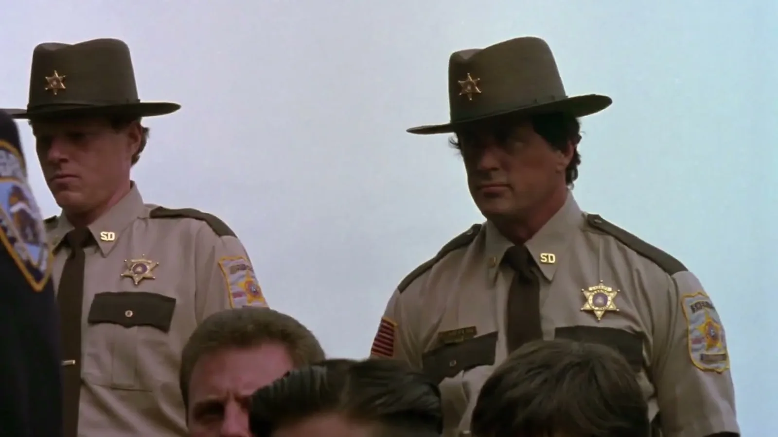 Sylvester Stallone de chapéu e uniforme de xerife ao lado de outro policial em cena de Cop Land