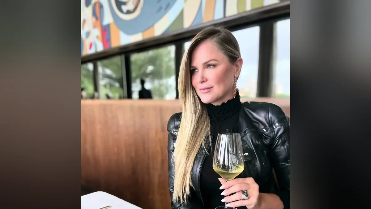 Susana Werner, de jaqueta de couro preta e cabelo loiro comprido, segura uma taça de vinho branco num restaurante