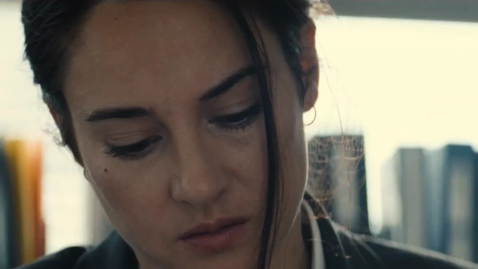 Shailene Woodley, de cabelo preso e blazer escuro, olha para baixo numa sala com livros, no papel da agente do FBI Joanne Miller