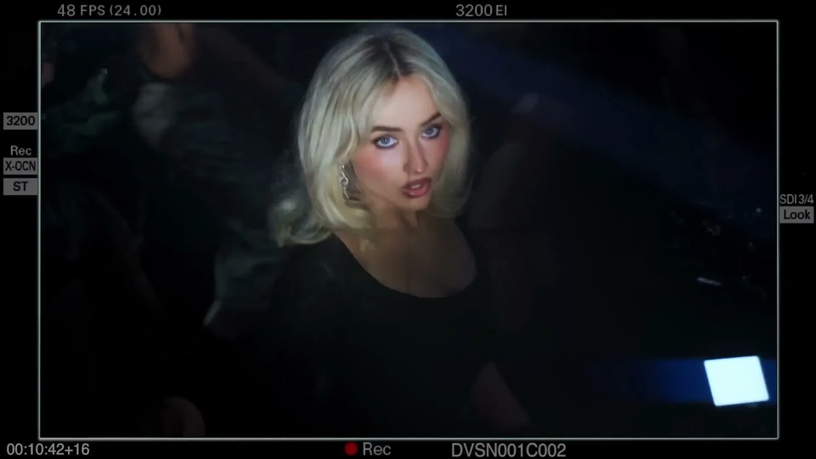 Sabrina Carpenter, de cabelo loiro e roupa preta, olhando para a câmera no clipe de Bring Your Love