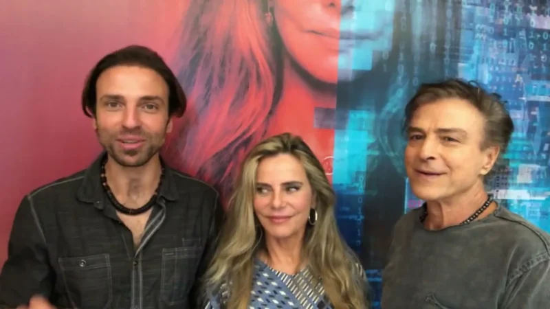 Kim Riccelli, Bruna Lombardi e Carlos Alberto Riccelli sorrindo lado a lado diante de um painel colorido