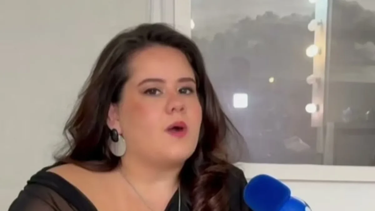 Karol Lannes, de cabelo escuro e brinco prateado, fala durante uma entrevista