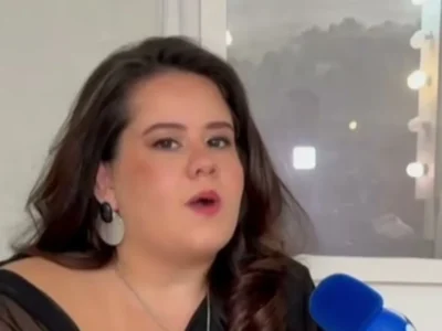 Karol Lannes, de cabelo escuro e brinco prateado, fala durante uma entrevista