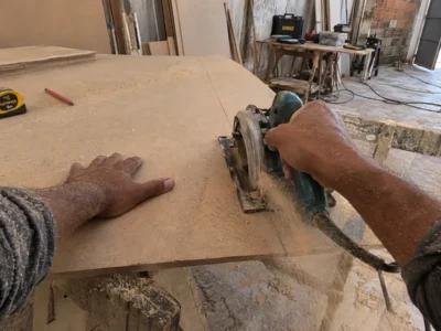 Mãos cortando uma chapa de MDF com serra circular numa oficina de marcenaria, vistas do ponto de vista de quem trabalha