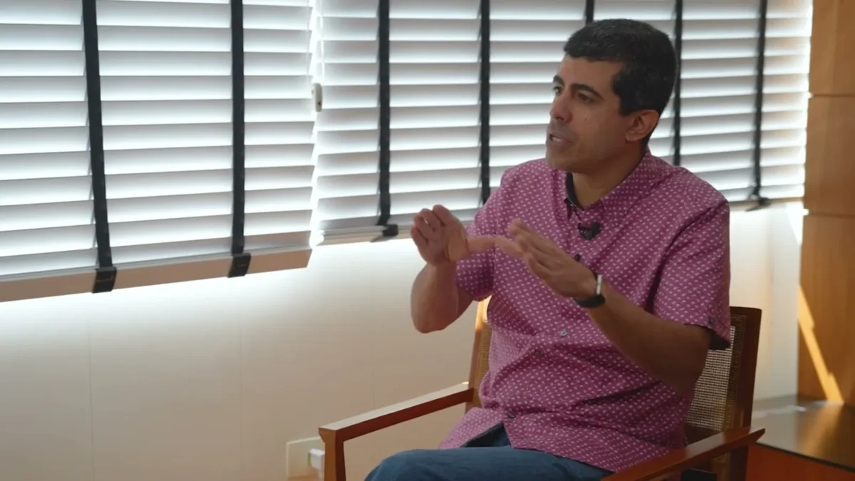 Marcius Melhem, de camisa estampada, sentado e gesticulando durante uma entrevista