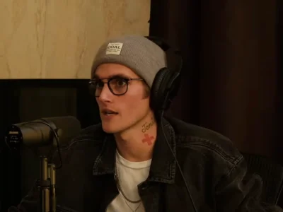 Presley Gerber, de gorro cinza, óculos de grau e fone de ouvido, fala num estúdio de podcast