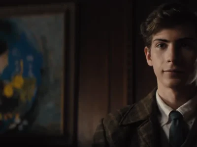 Jacob Tremblay, de terno e gravata, como o jovem Ted Kaczynski numa sala com paredes de madeira, em cena de Unabomber