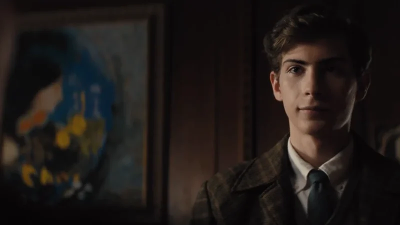 Jacob Tremblay, de terno e gravata, como o jovem Ted Kaczynski numa sala com paredes de madeira, em cena de Unabomber