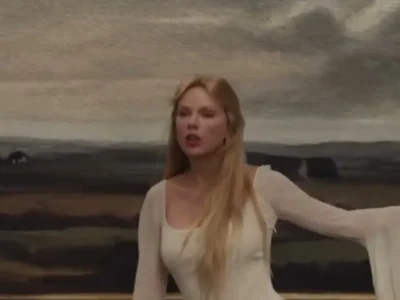 Taylor Swift de vestido branco e cabelo loiro comprido, de braço aberto, no clipe de The Fate of Ophelia