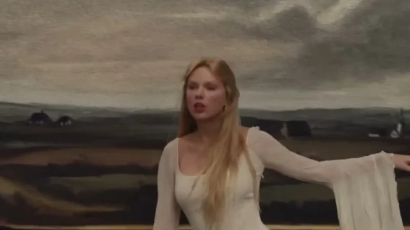 Taylor Swift de vestido branco e cabelo loiro comprido, de braço aberto, no clipe de The Fate of Ophelia